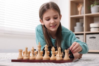 Cute girl playing chess on floor in room