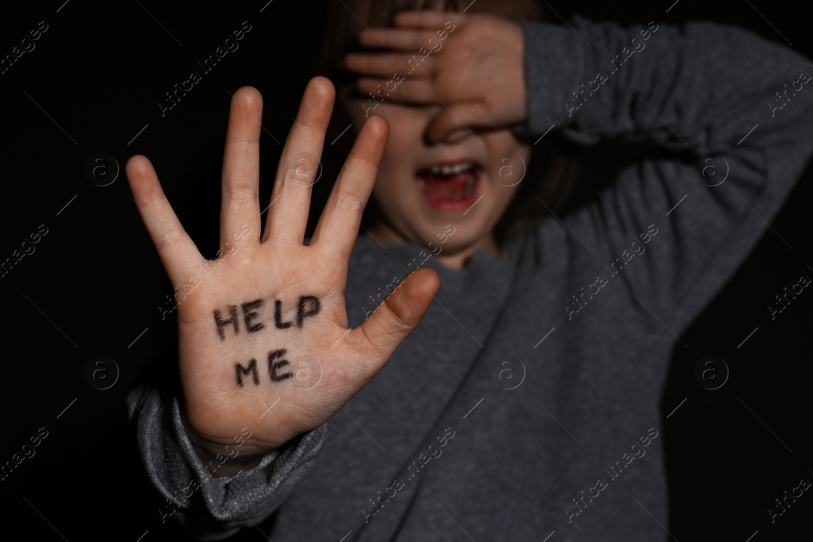 Photo of Abused little girl showing palm with phrase HELP ME on black background, focus on hand. Domestic violence concept
