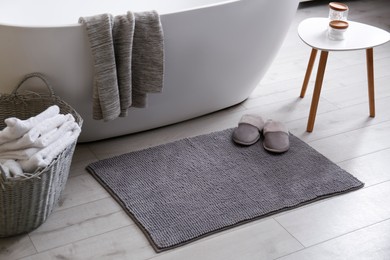 Photo of Soft grey mat with slippers on floor near tub in bathroom. Interior design