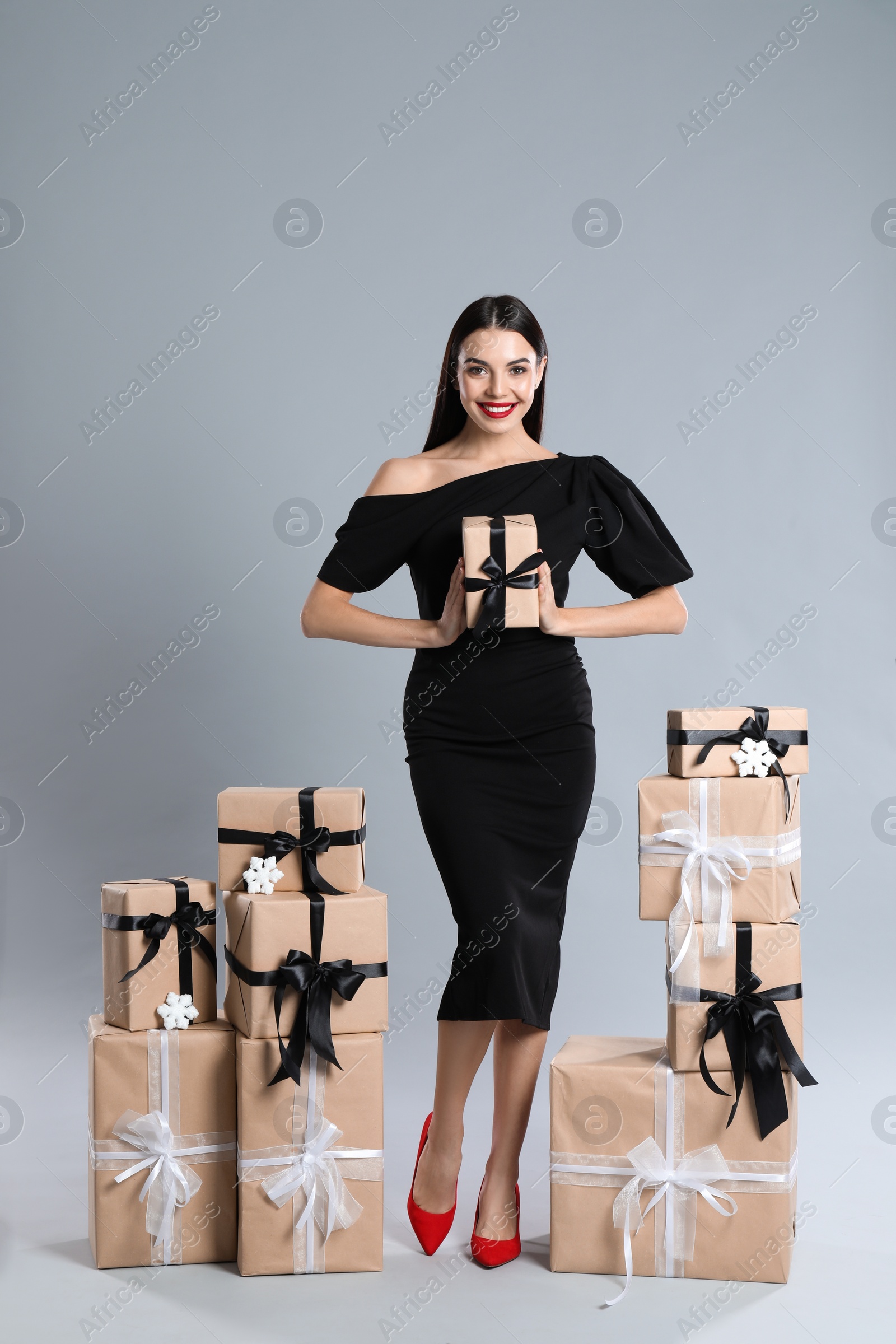 Photo of Woman in black dress with Christmas gifts on grey background