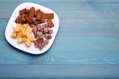 Photo of Toothpick appetizers. Pieces of sausage, cheese and croutons on light blue wooden table, top view. Space for text