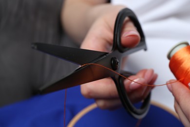 Photo of Woman cutting thread on blurred background, closeup