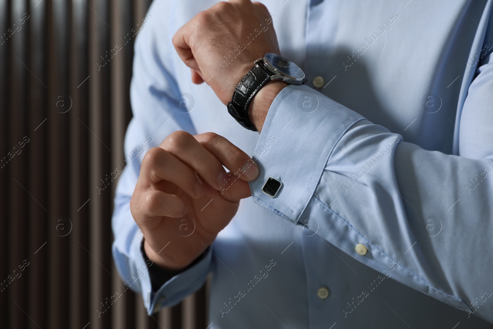 Photo of Stylish man putting on cufflink near wooden wall, closeup