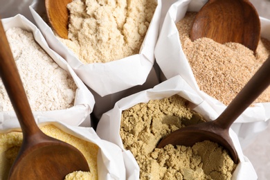 Photo of Paper bags with different types of flour and wooden spoons, closeup