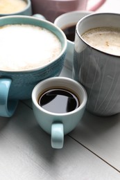 Many different cups with aromatic hot coffee on white wooden table