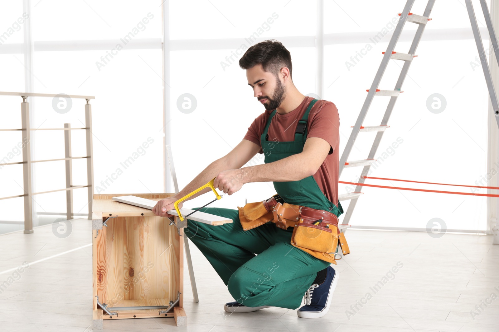 Photo of Carpenter in uniform making furniture indoors. Professional construction tools