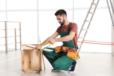 Carpenter in uniform making furniture indoors. Professional construction tools