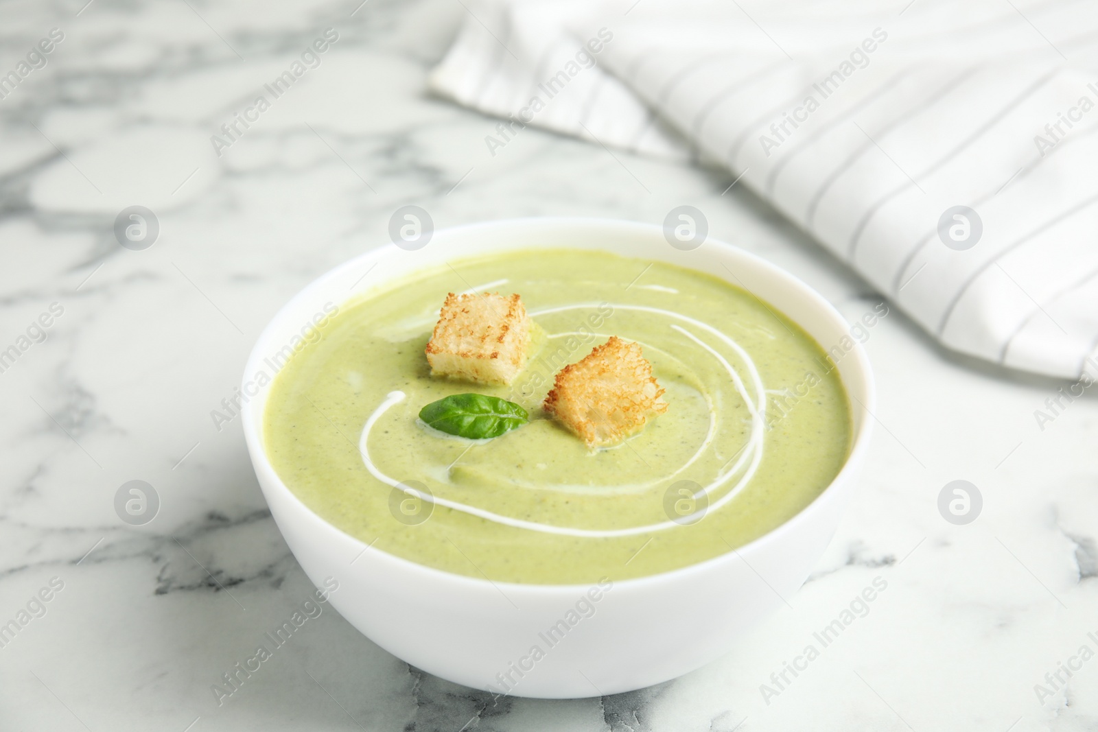 Photo of Delicious broccoli cream soup with croutons served on white marble table