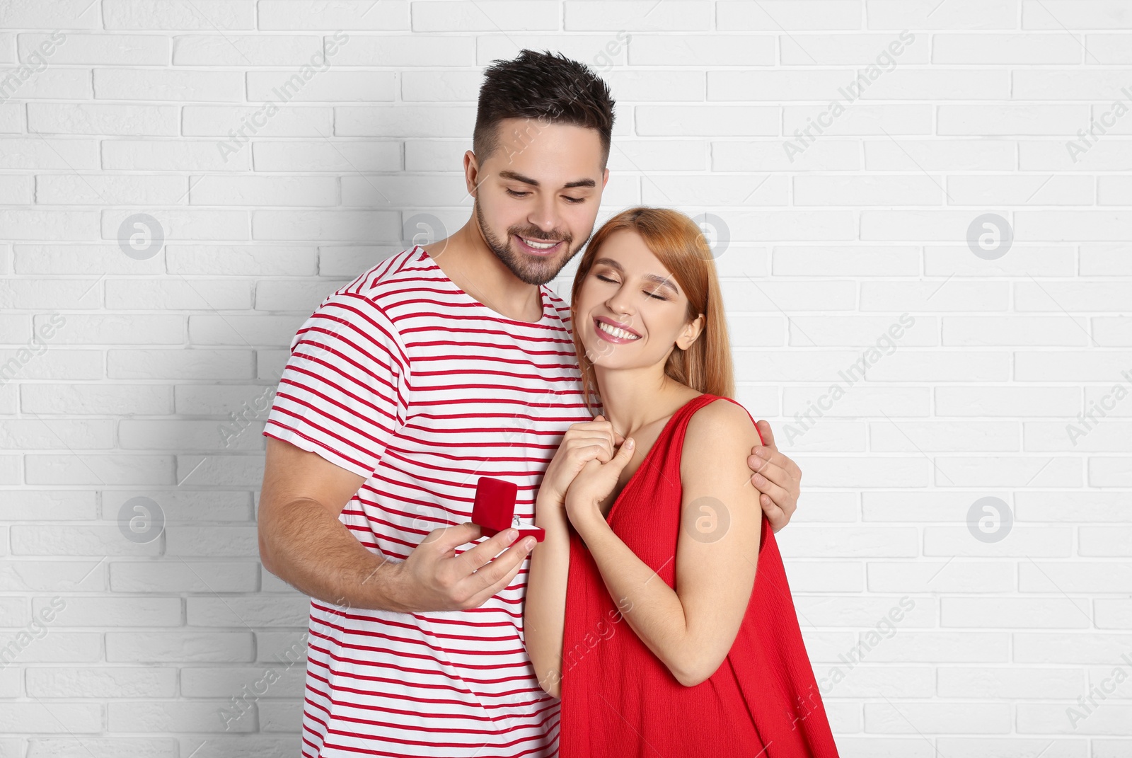 Photo of Man with engagement ring making marriage proposal to girlfriend near white brick wall