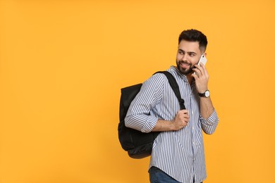 Photo of Young man with stylish backpack talking on phone against yellow background. Space for text