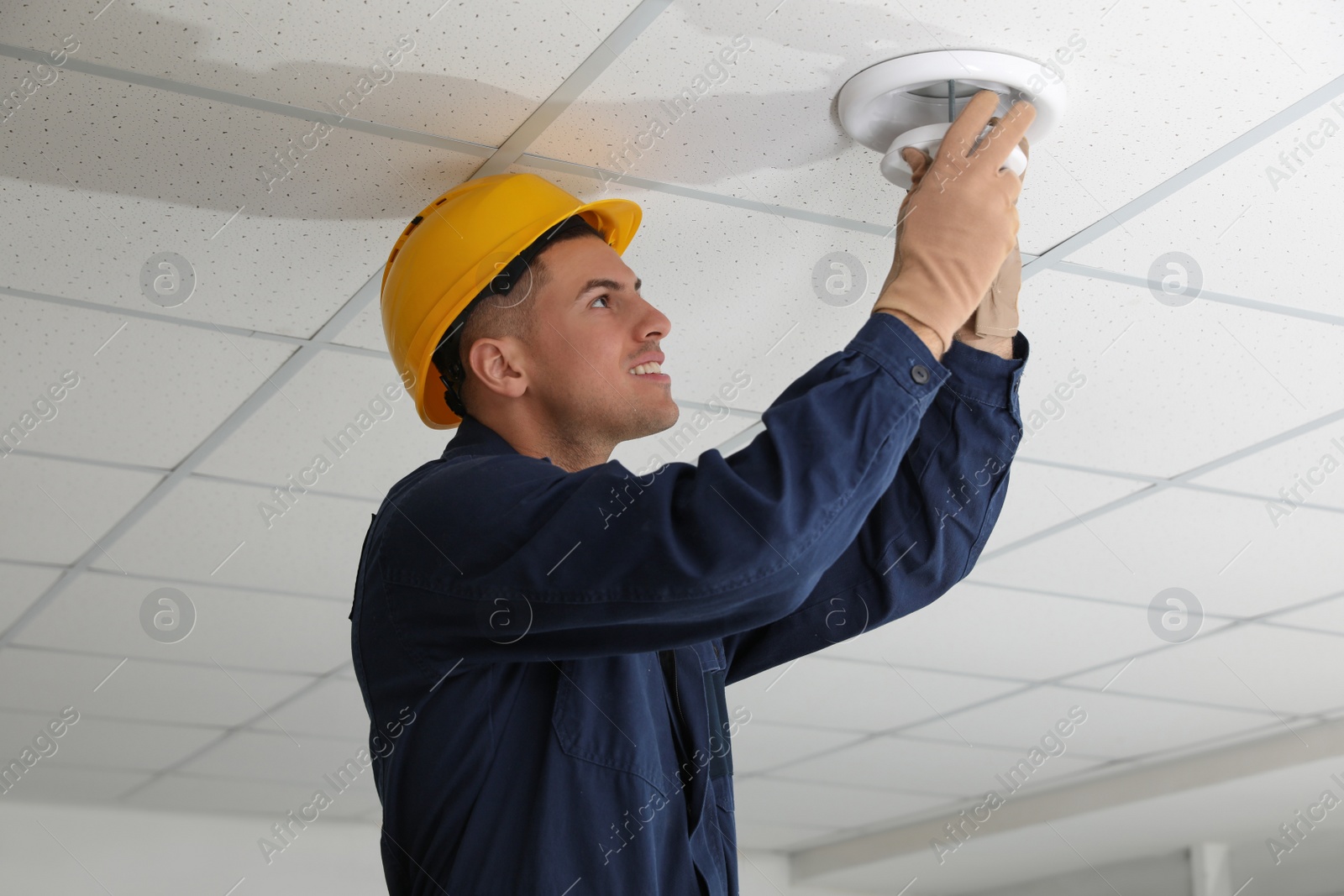 Photo of Electrician in uniform repairing ceiling lamp indoors