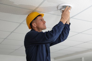 Photo of Electrician in uniform repairing ceiling lamp indoors