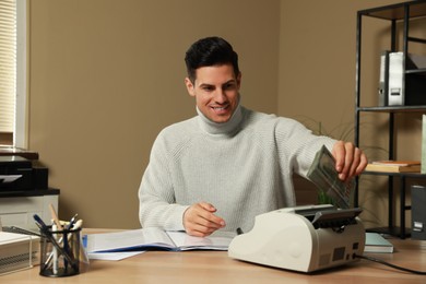 Man putting money into banknote counter at wooden table indoors