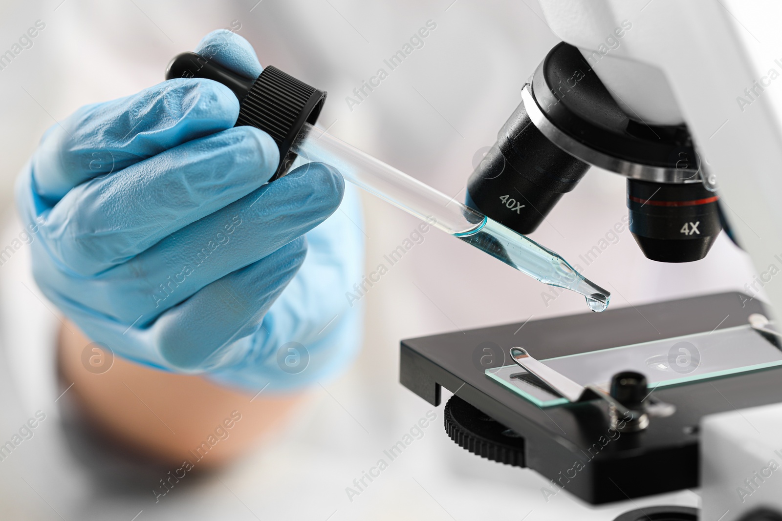 Photo of Scientist working with light blue liquid and microscope, closeup