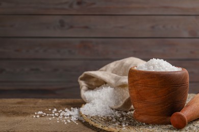 Photo of Pestle and mortar with natural sea salt on wooden table, space for text