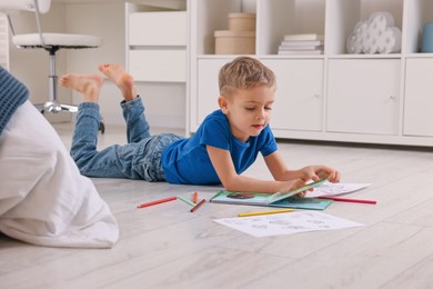 Photo of Cute little boy reading book on warm floor at home. Heating system