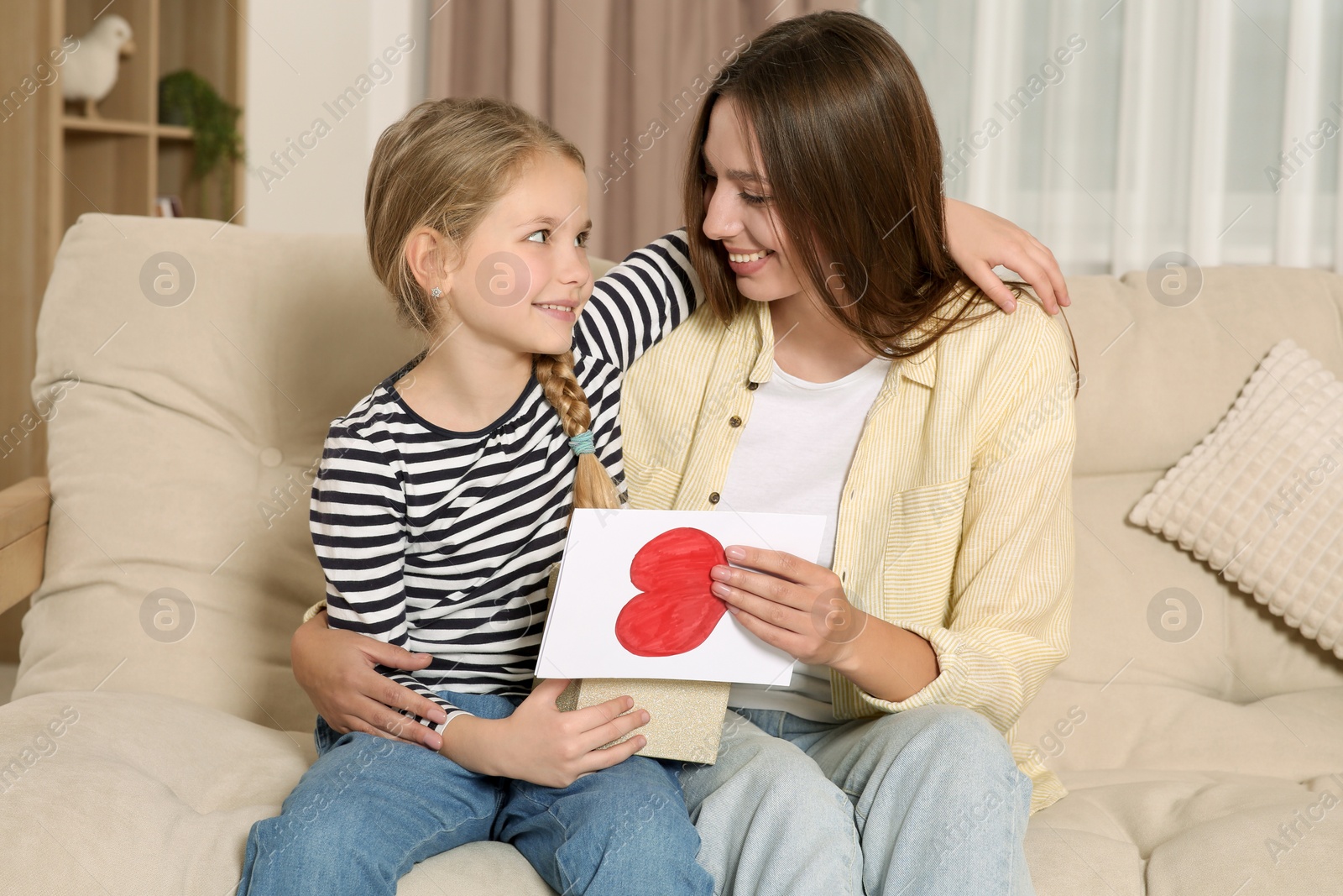 Photo of Young woman and her daughter with gifts on sofa at home