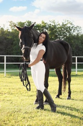 Photo of Young woman in horse riding suit and her beautiful pet outdoors on sunny day