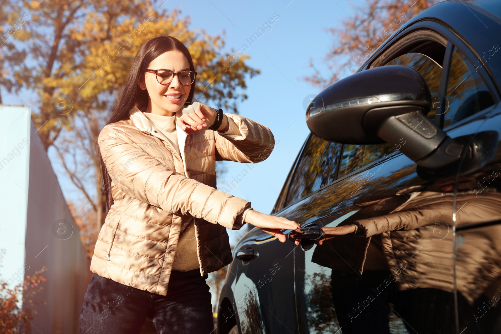 Photo of Emotional woman checking time on watch near car. Being late concept