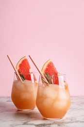 Glasses of grapefruit cocktails on table against color background. Space for text