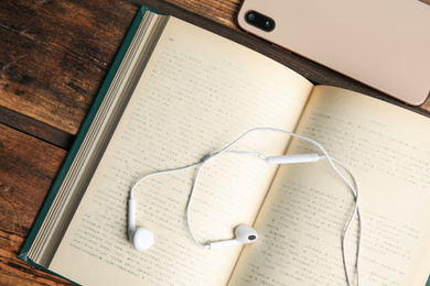 Photo of Book, headphones and smartphone on wooden table, closeup