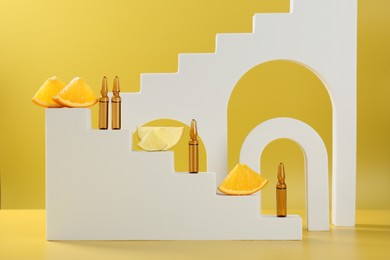 Stylish presentation of skincare ampoules with vitamin C and citrus slices on yellow background