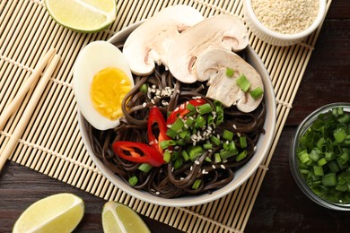 Photo of Tasty buckwheat noodles (soba) with chili pepper, sesame, onion, egg and chopsticks on wooden table, flat lay