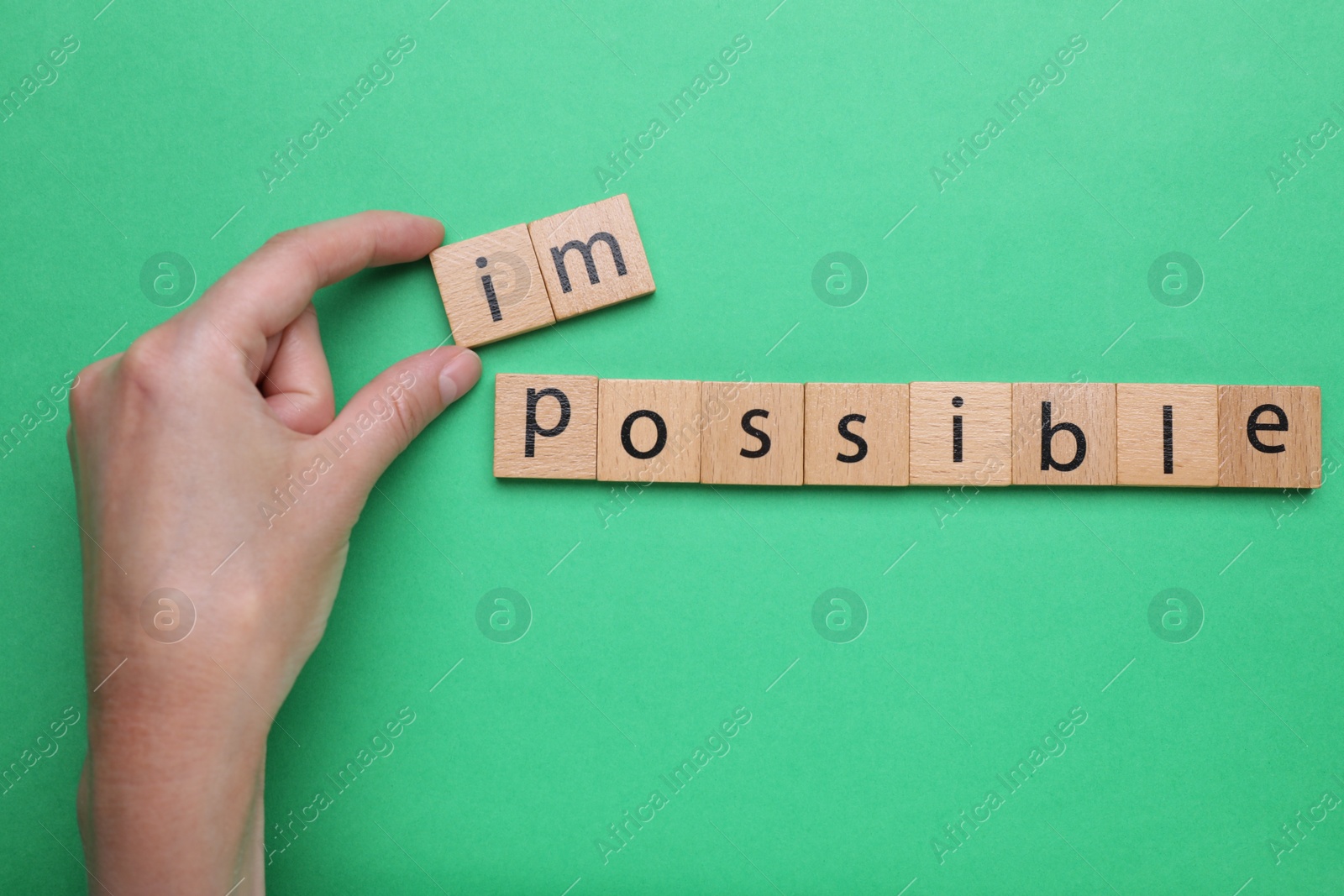 Photo of Motivation concept. Woman changing word from Impossible into Possible by removing wooden squares on green background, top view