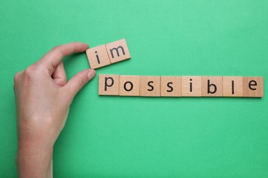 Photo of Motivation concept. Woman changing word from Impossible into Possible by removing wooden squares on green background, top view