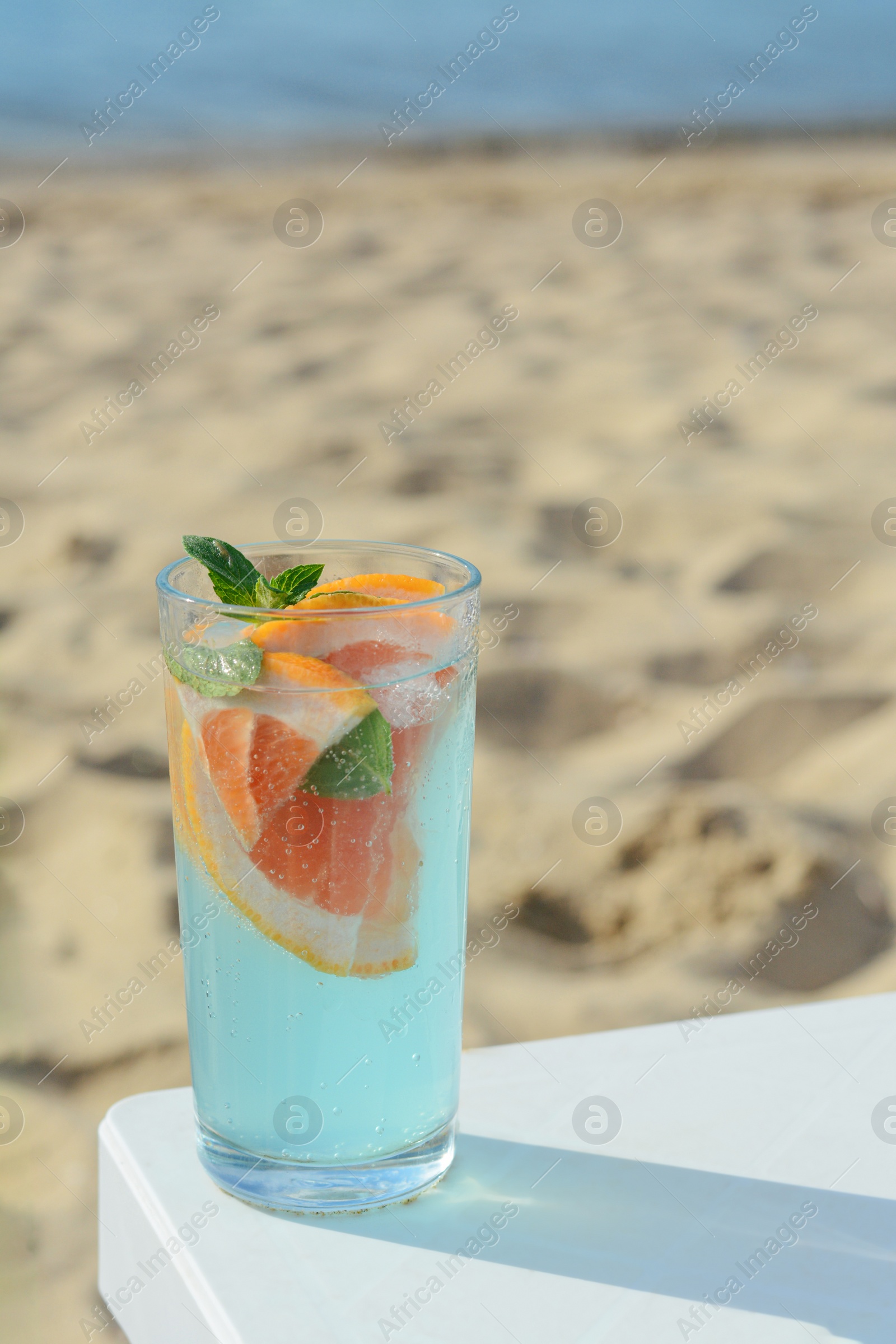 Photo of Glass of refreshing drink with grapefruit and mint on white table at beach