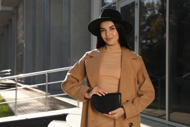 Beautiful young woman with stylish waist bag on city street, space for text