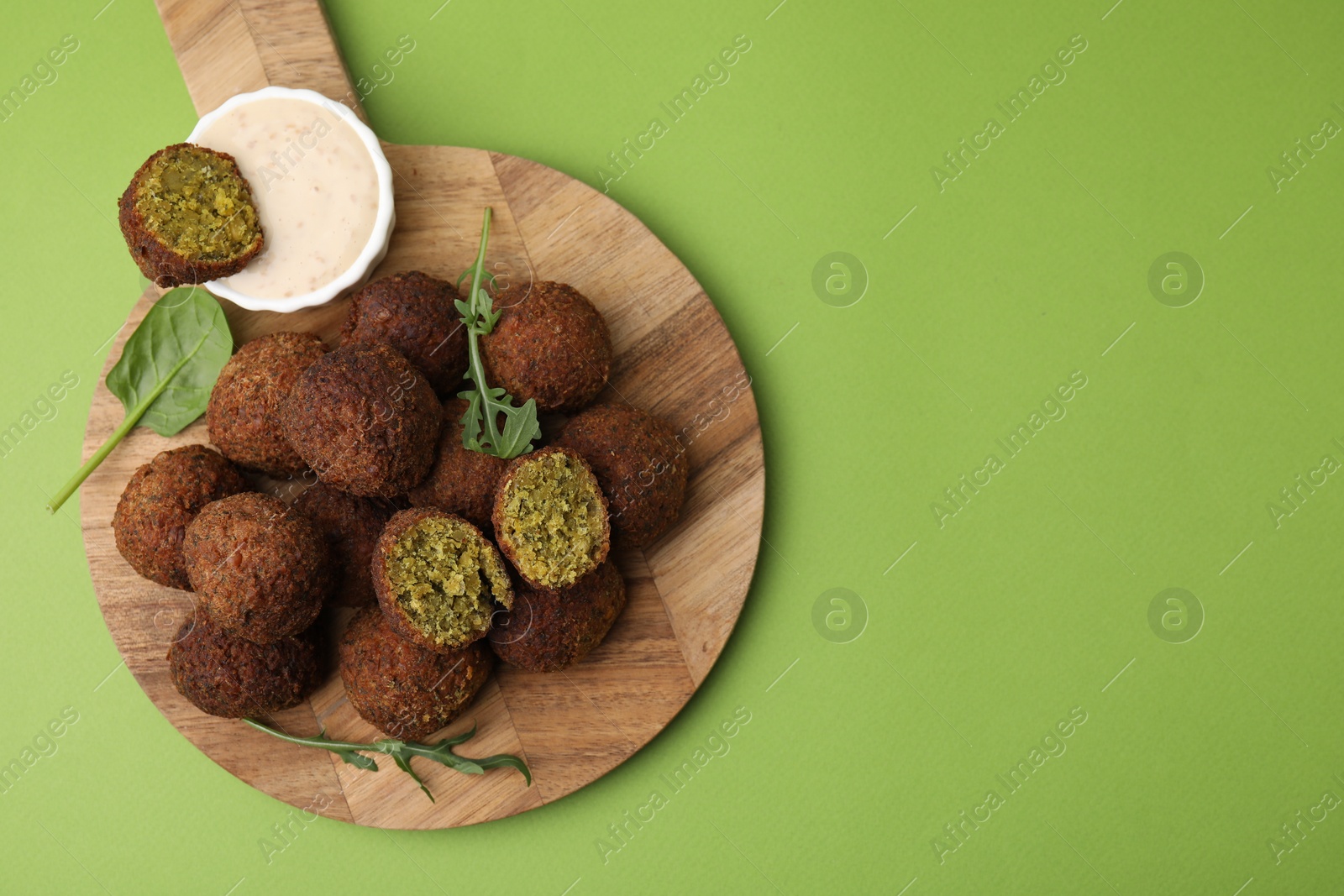 Photo of Delicious falafel balls, herbs and sauce on green background, top view. Space for text