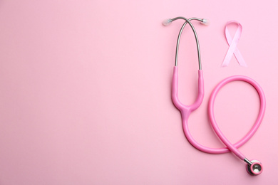 Photo of Pink ribbon as breast cancer awareness symbol and stethoscope on color background, flat lay. Space for text