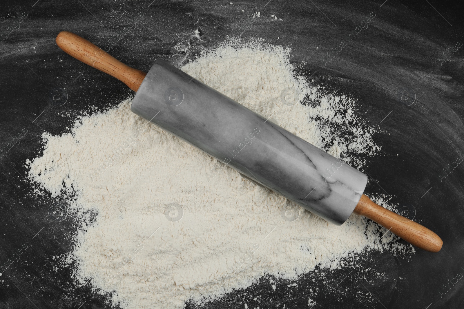 Photo of Flour and rolling pin on black table, top view