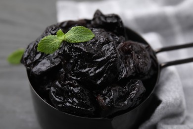 Photo of Sweet dried prunes and mint in scoop on grey table, closeup