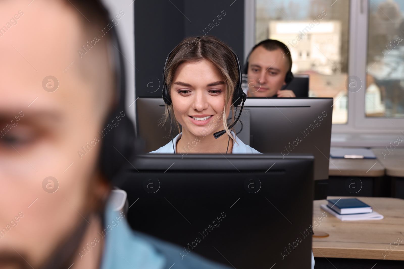 Photo of Call center operators working in modern office, focus on young woman with headset