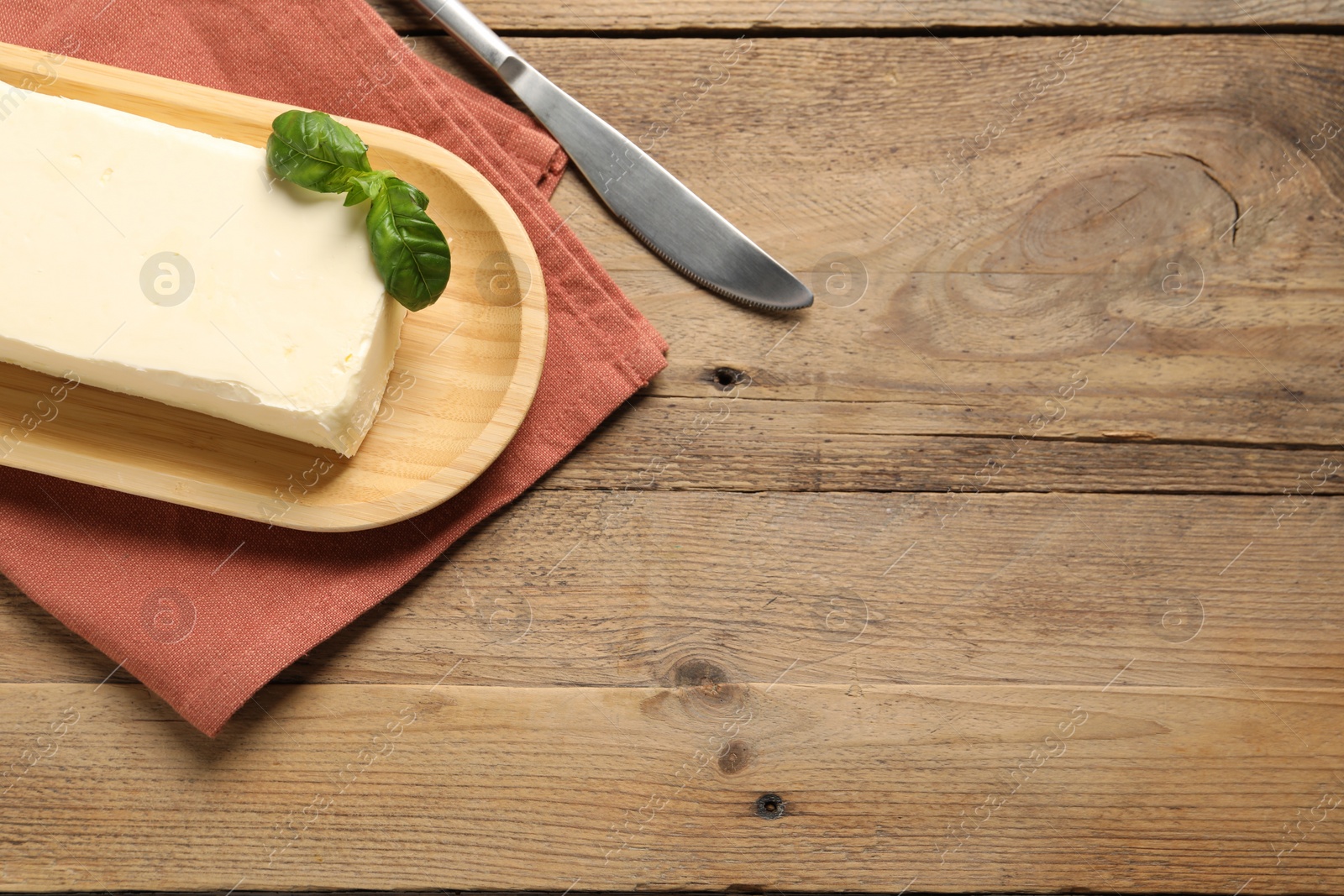 Photo of Block of tasty butter with basil and knife on wooden table, top view. Space for text