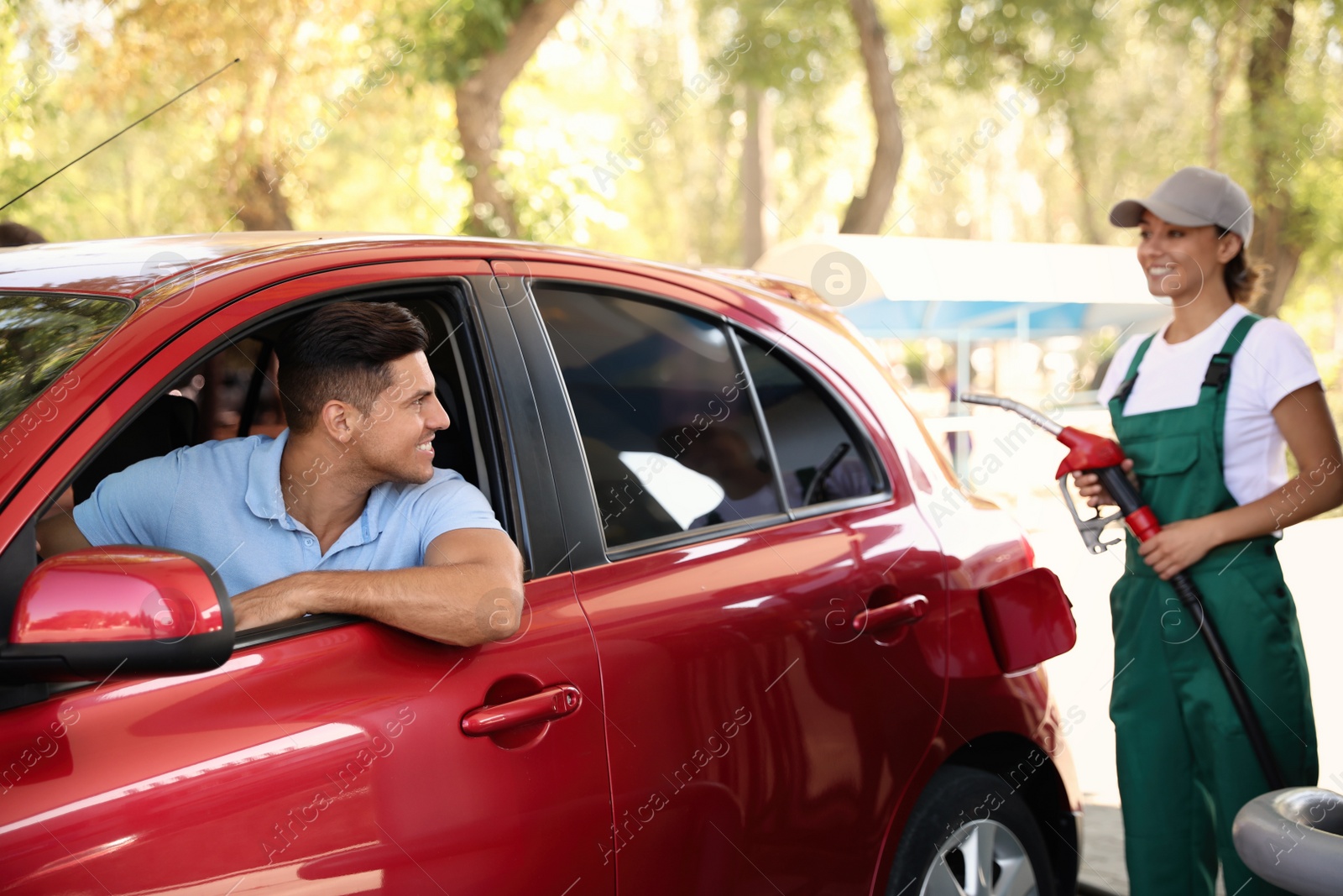 Photo of Man sitting in car while young worker refueling his auto at modern gas station