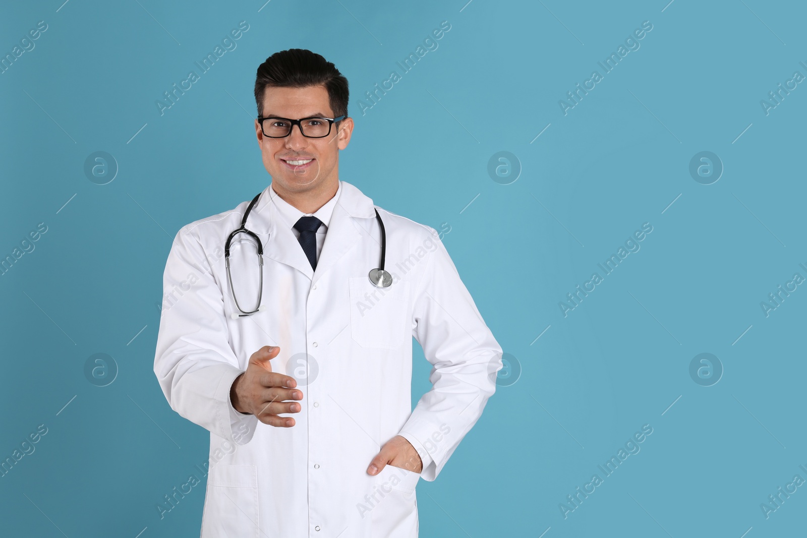 Photo of Happy male doctor offering handshake on light blue background. Space for text