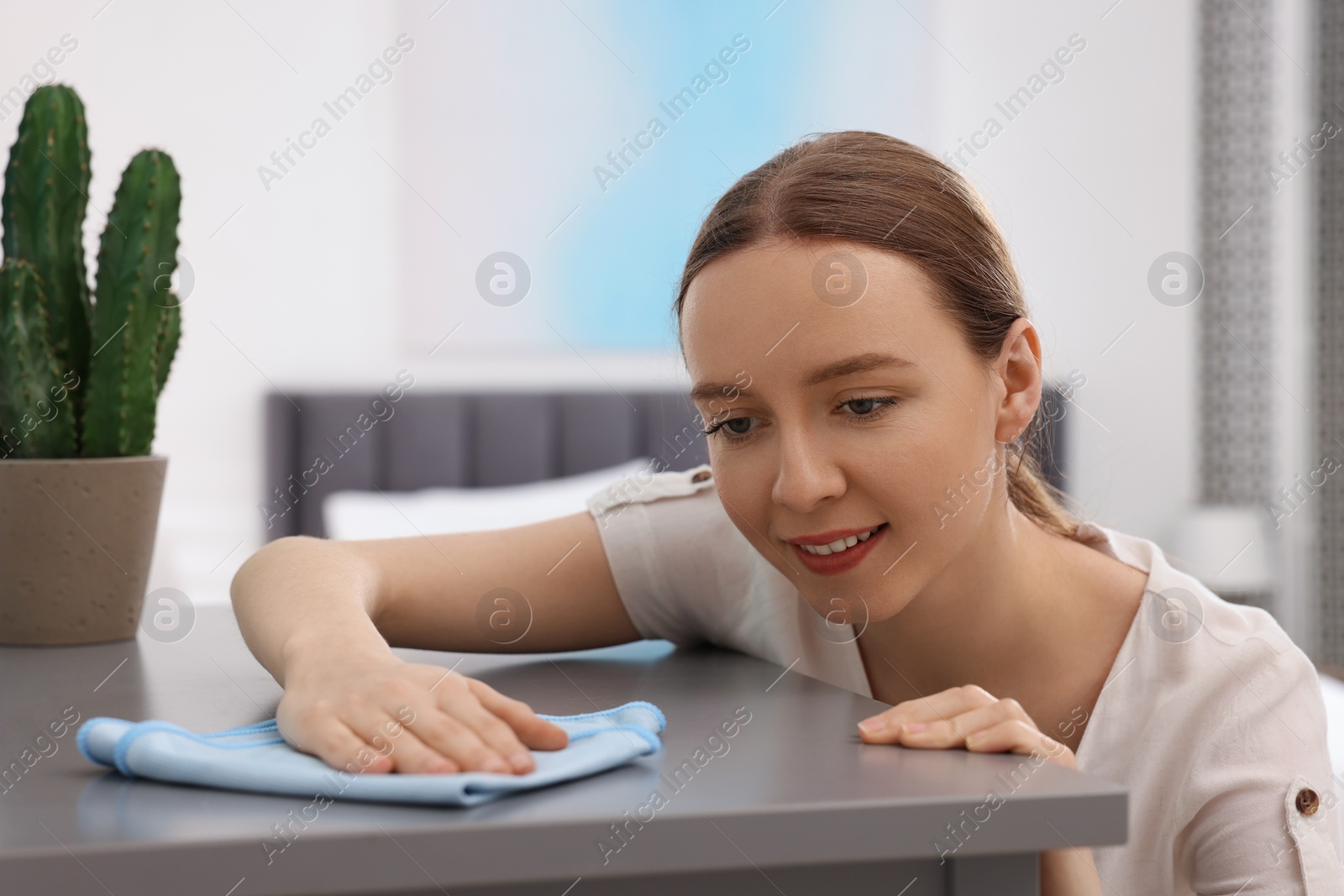 Photo of Woman with microfiber cloth cleaning grey chest of drawers in room