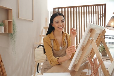 Photo of Young woman drawing on easel with pencil at table indoors