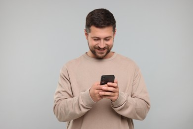 Photo of Happy man using smartphone on light grey background