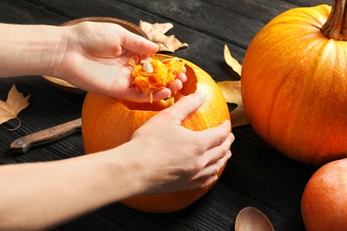 Photo of Woman making Halloween pumpkin head jack lantern on wooden table, closeup