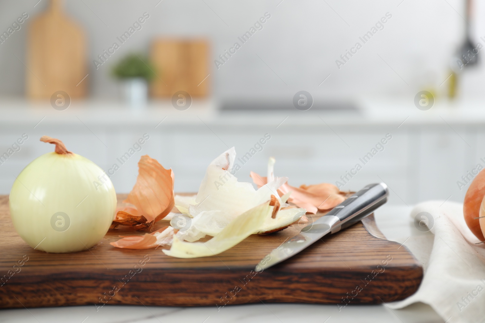 Photo of Wooden board with fresh onion and peels on white marble table in kitchen, closeup