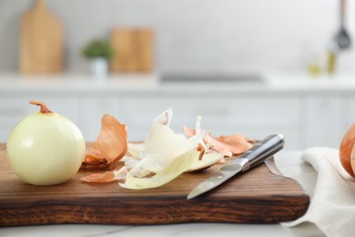 Photo of Wooden board with fresh onion and peels on white marble table in kitchen, closeup
