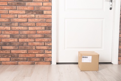 Photo of Cardboard parcel box on floor near apartment entrance. Mockup for design