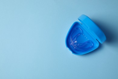Photo of Transparent dental mouth guard in container on light blue background, top view with space for text. Bite correction