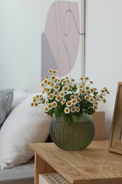Photo of Beautiful bouquet of chamomile flowers on wooden nightstand in bedroom. Stylish interior
