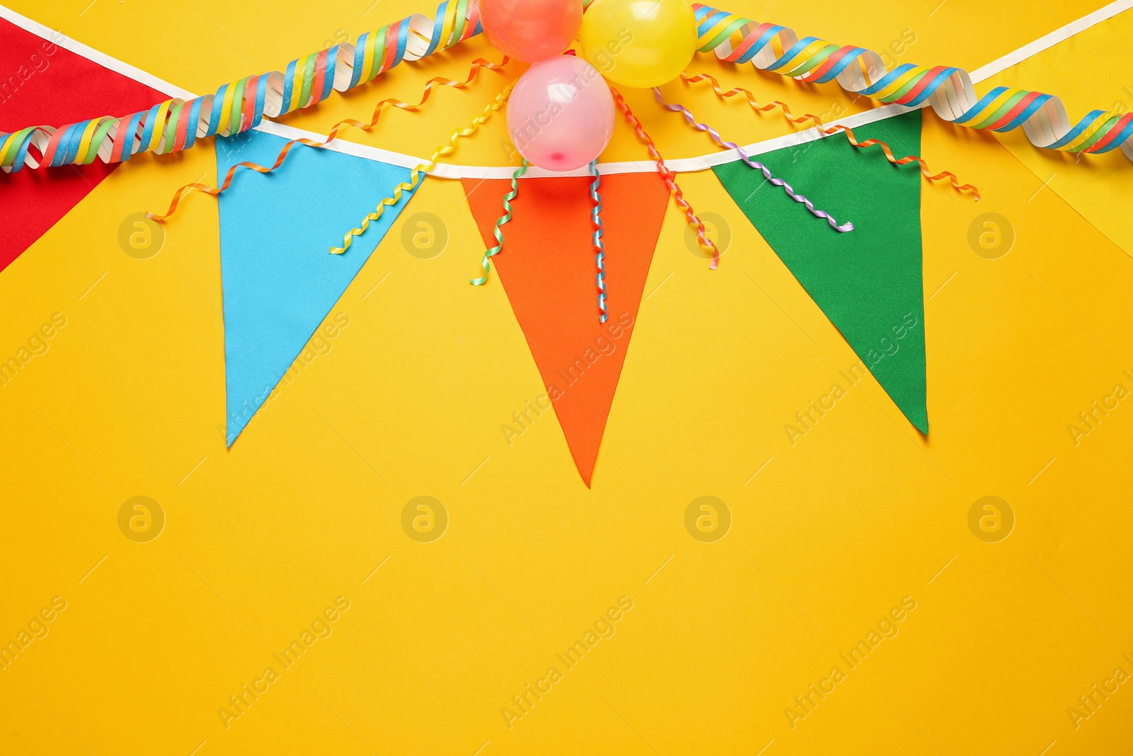 Photo of Bunting with colorful triangular flags and other festive decor on yellow background, flat lay. Space for text