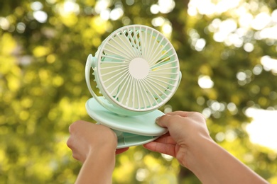 Woman holding portable fan outdoors on sunny summer day, closeup